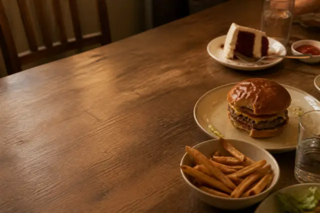A shared table with a burger, fries and a slice of cake in warm indoor light.