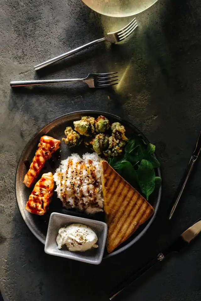 A plated dinner of grilled salmon, rice, and leafy greens on a dark wood table.