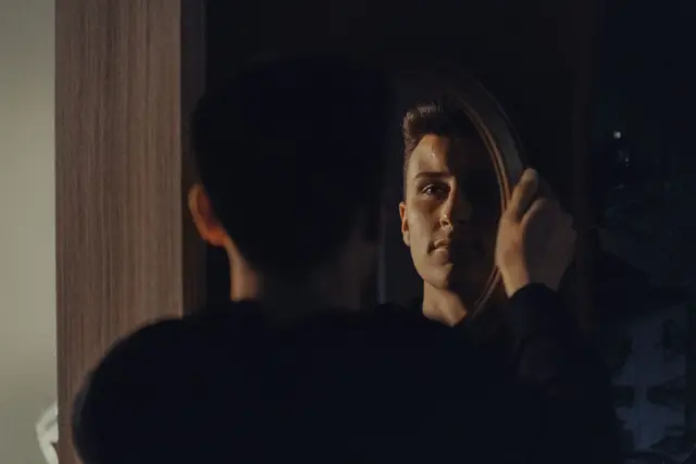 A person standing in front of a mirror in soft morning light.
