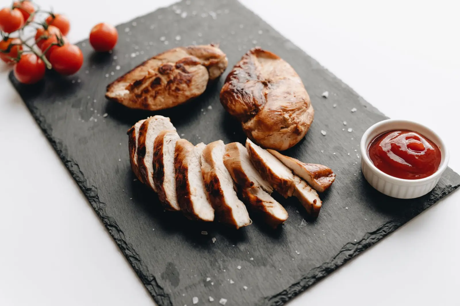 Sliced grilled chicken breast on a slate board with cherry tomatoes.