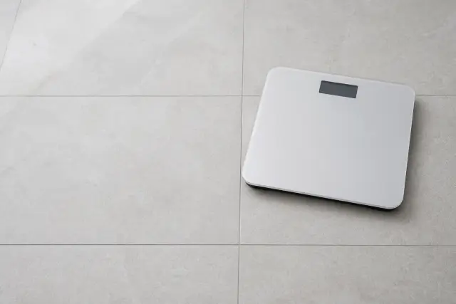 A floor scale on plain tiles in flat morning daylight, seen from a high angle.