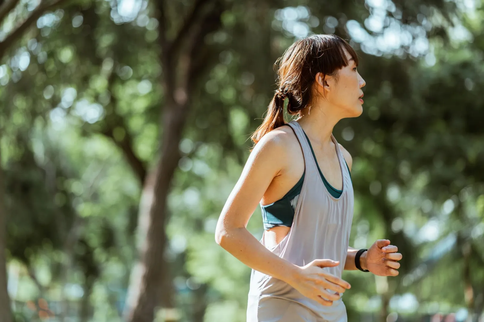 A woman jogging on a sunny morning through a green park.