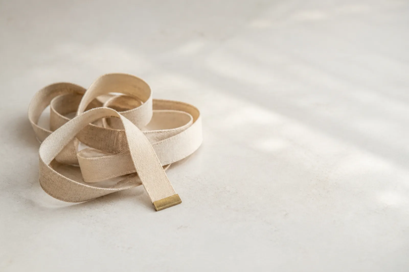 A tape measure coiled on a plain pale surface in soft daylight.