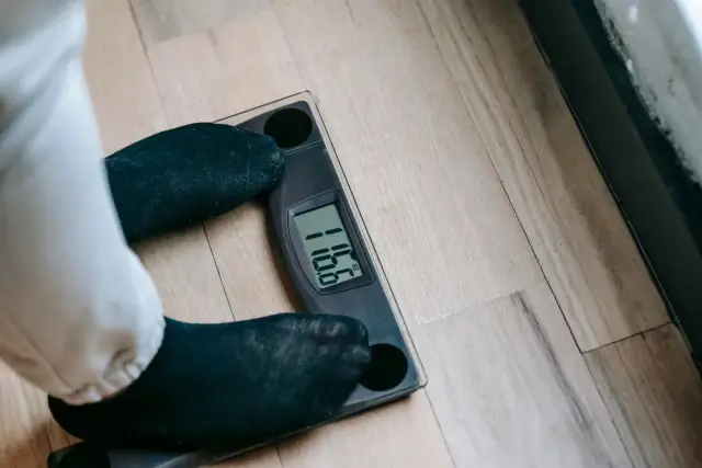 A person in socks standing on a digital bathroom scale, checking their weight.