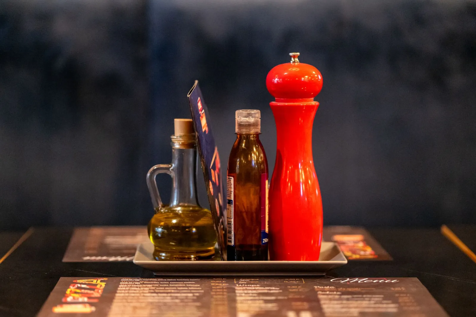 Bottles of olive oil and vinegar beside a pepper grinder on a restaurant table.
