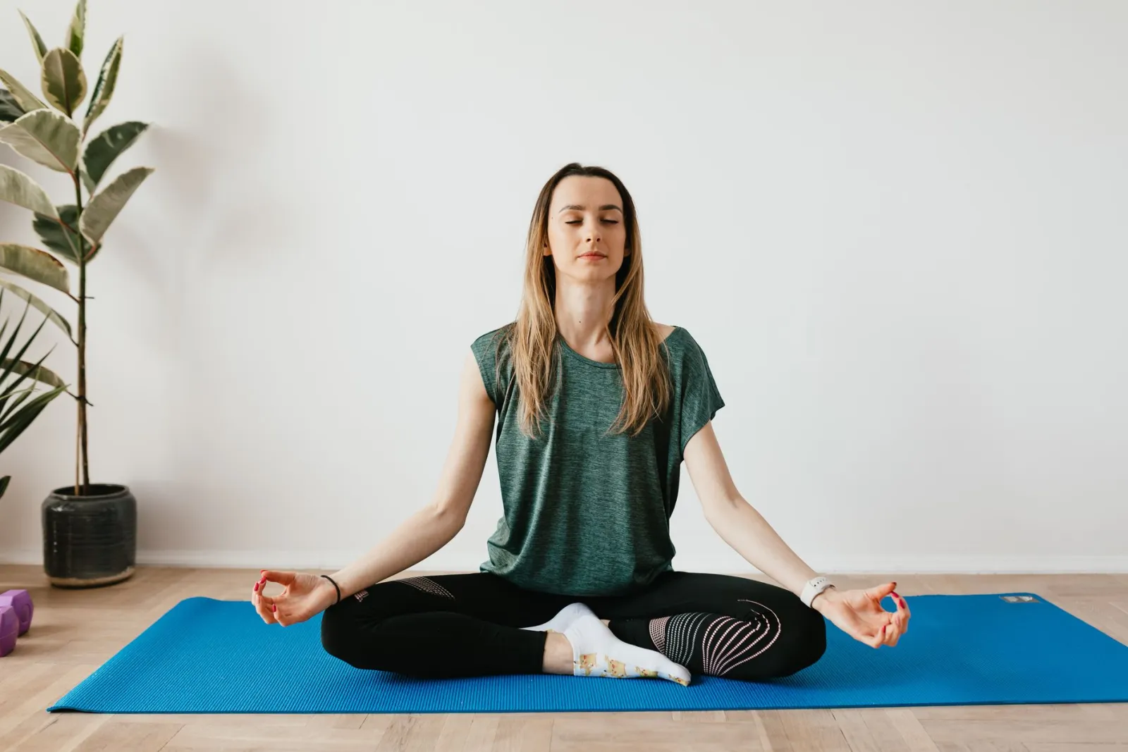 A woman meditating calmly on a mat at home.