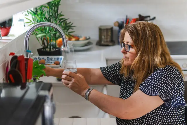 A middle-aged woman filling a glass with water in a modern kitchen setting.