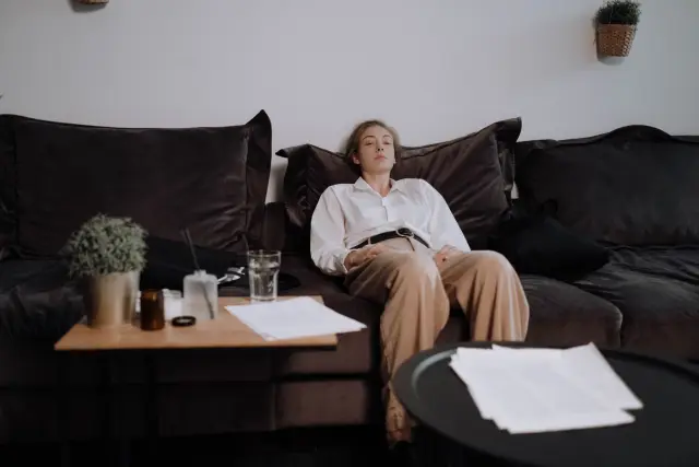 A woman sits tiredly on a couch in a living room, reflecting introspection.