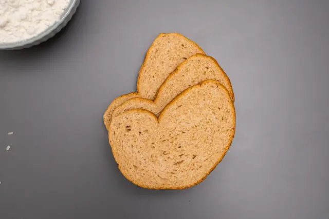 Slices of brown bread and a dusting of flour laid out on a table, seen from above.