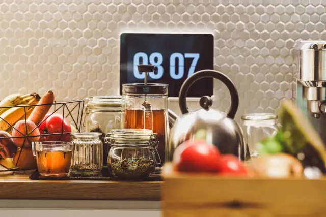 A cozy kitchen counter with tea, fruits, and a digital clock creating a warm domestic ambiance.