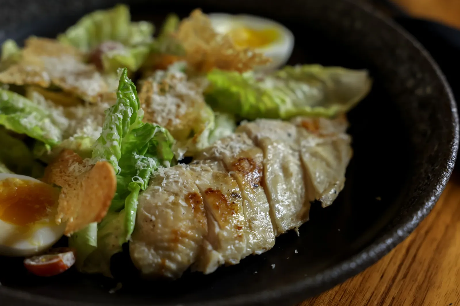 A plated meal of grilled chicken, mixed greens, and a boiled egg on a kitchen counter.