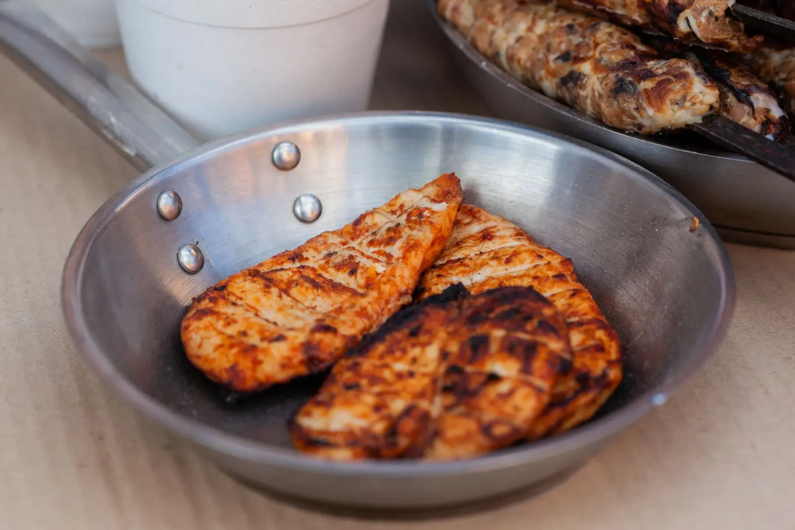 Seasoned chicken breasts grilled and served in a stainless steel pan.