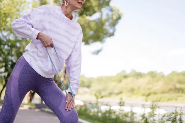 An older woman doing a resistance band workout outdoors.