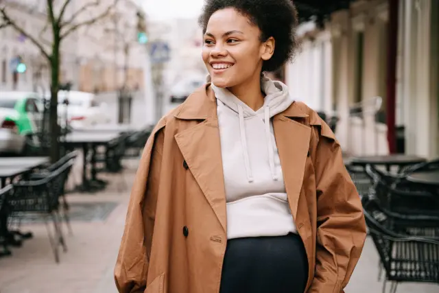 A smiling woman walking down a sunlit city street.