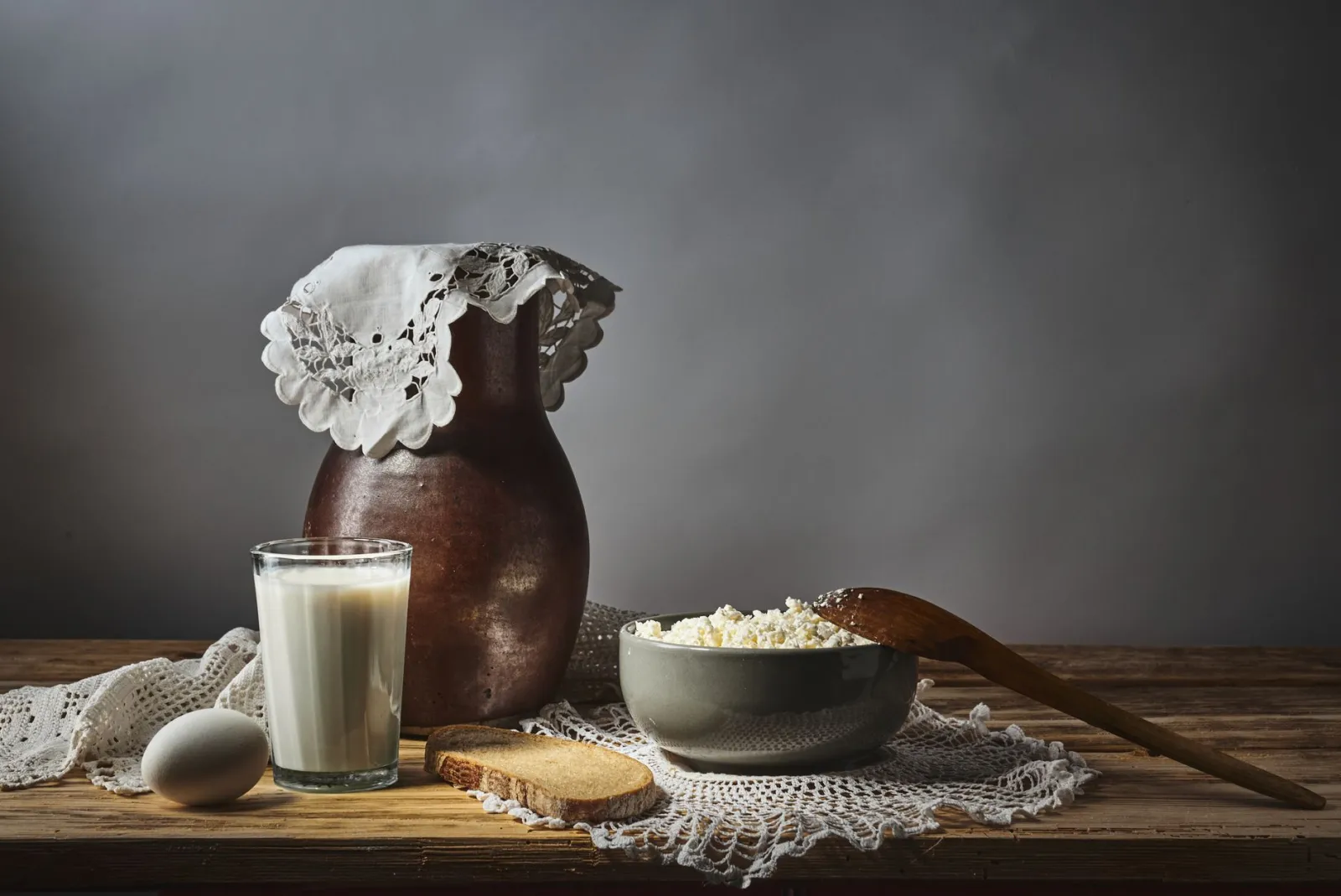 A rustic still life of milk, cottage cheese and bread on a wooden table.