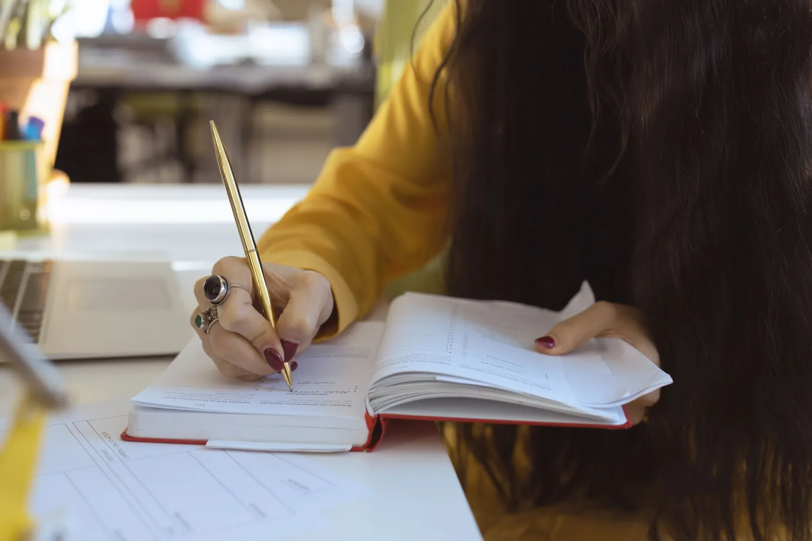 A woman writing in a notebook at a desk, focused on the page.