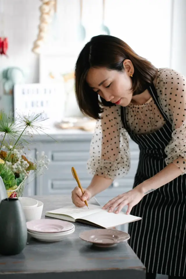 A woman writing in a notebook in a well-lit kitchen.
