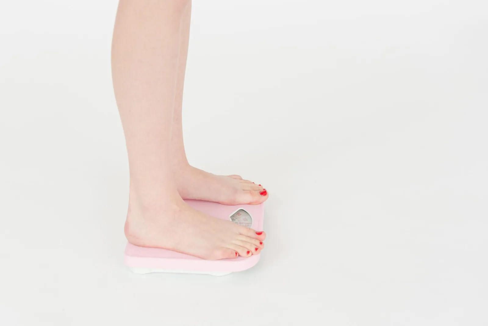 A woman standing on a bathroom scale, viewed from the side.