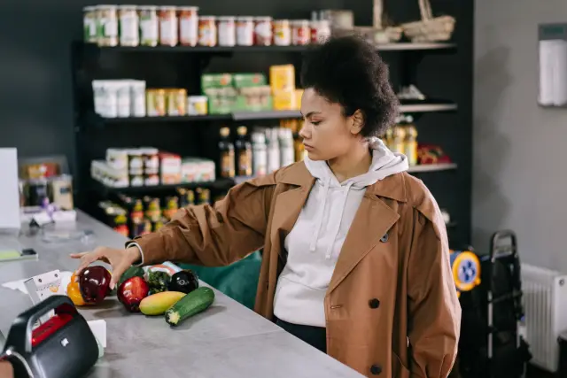 A woman selecting fresh fruits and vegetables at a grocery store with shelves stocked in the background.