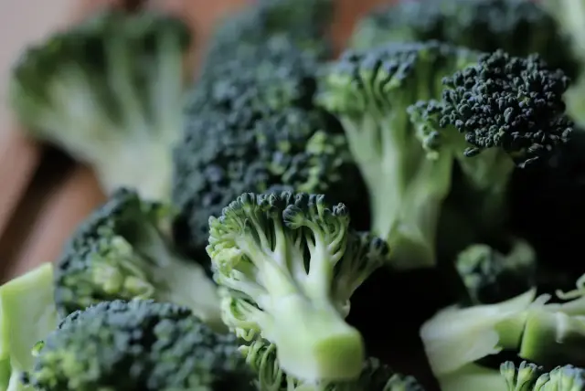 Fresh green broccoli florets on a wooden chopping board.