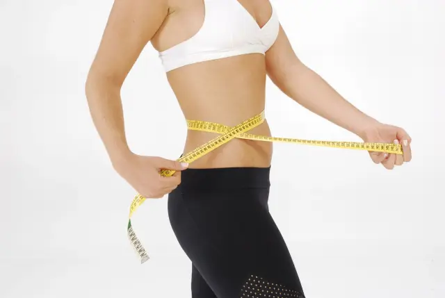 Fit woman in sportswear measuring her waist with a tape measure.