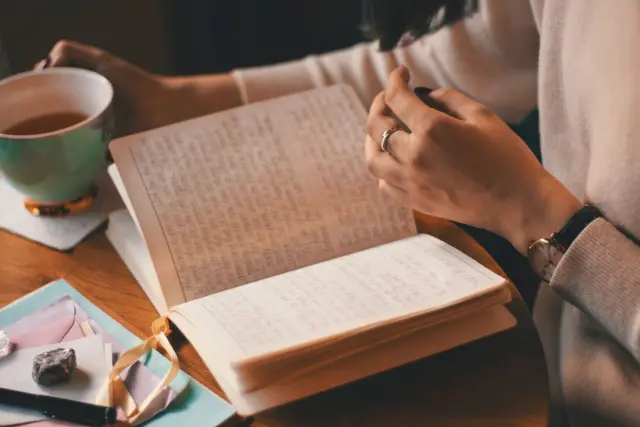 A person writing in a notebook at a sunlit desk.