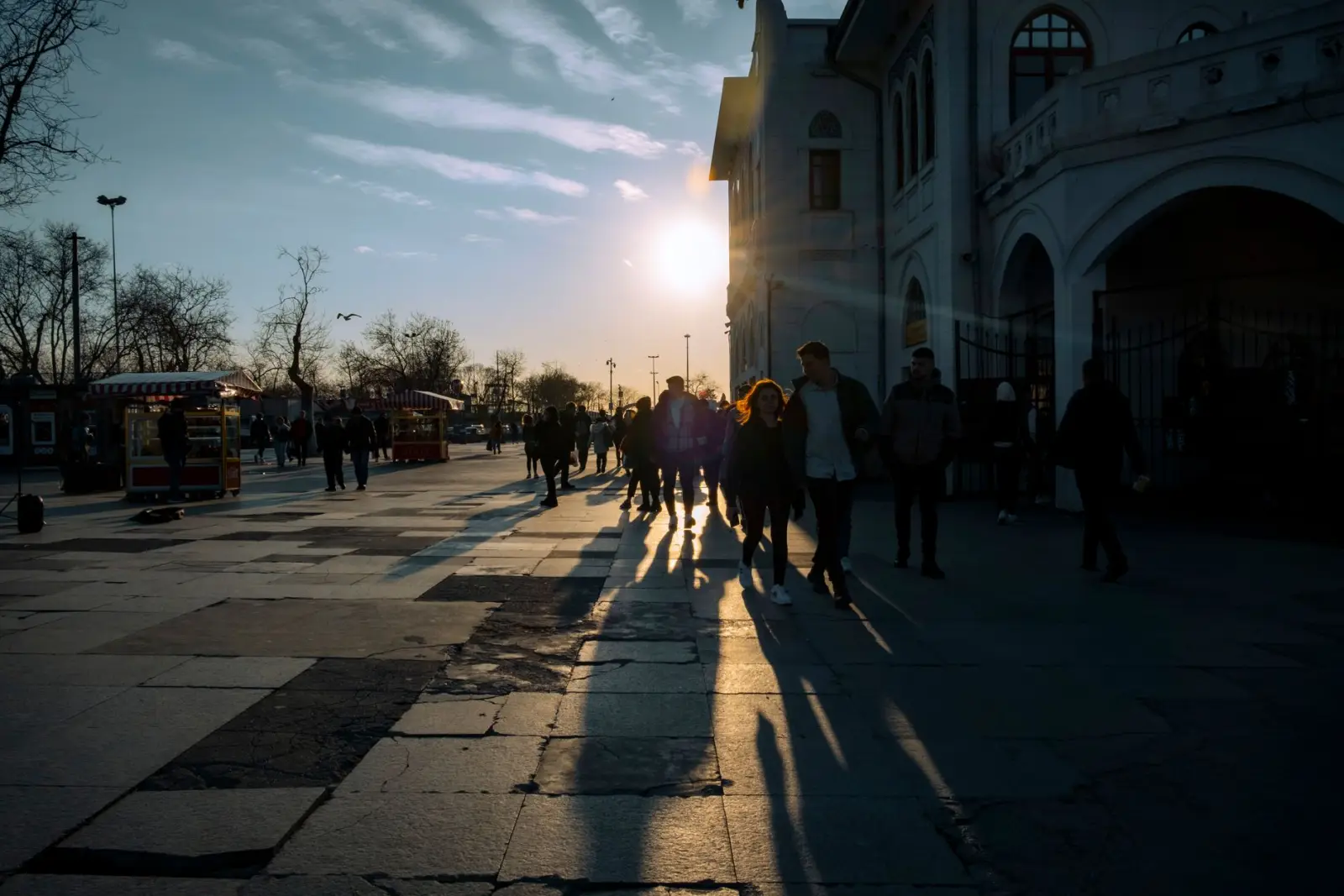 Anonymous pedestrians walking on a city pavement at golden hour, silhouetted with long shadows.