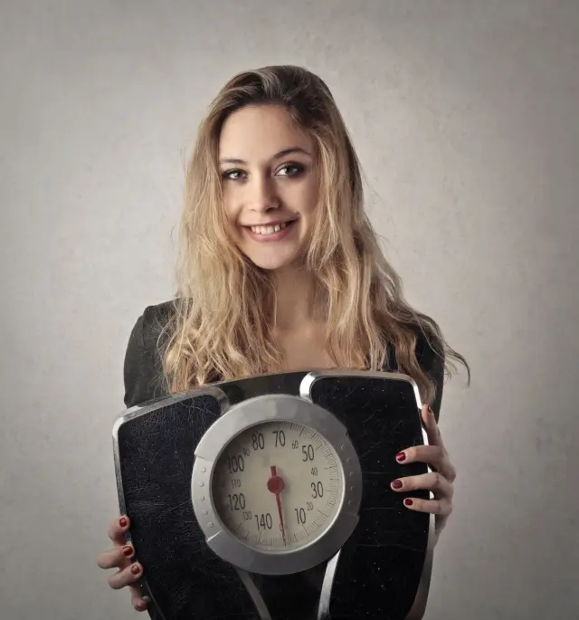 A young woman holding a vintage bathroom scale indoors.