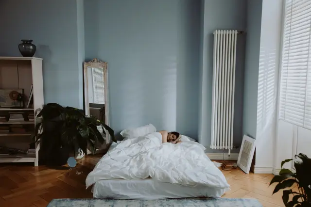 A person sleeping peacefully in a cozy, softly lit bedroom in early morning light.