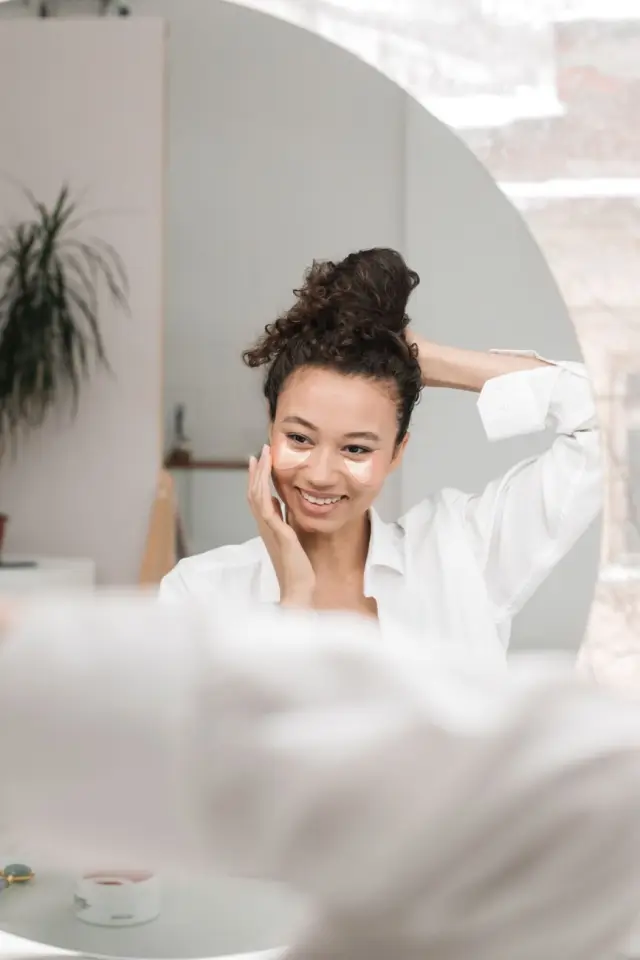 A woman smiling at her reflection during a morning skincare routine.