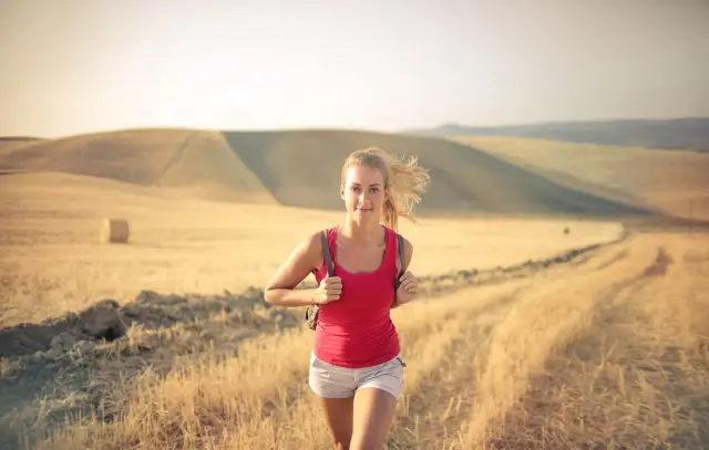 A woman jogging through a sunlit golden field.