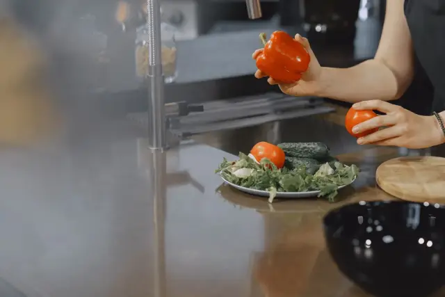A person slicing fresh vegetables on a cutting board in a bright modern kitchen.