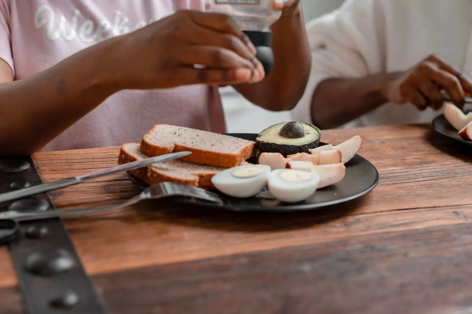 A wholesome breakfast plate with avocado, boiled eggs, and bread on a wooden table.