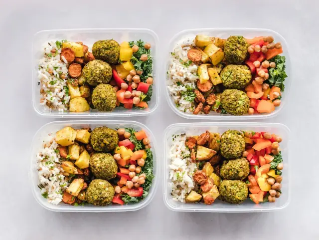 Colorful protein-forward meal-prep containers with grains and vegetables on a white surface.
