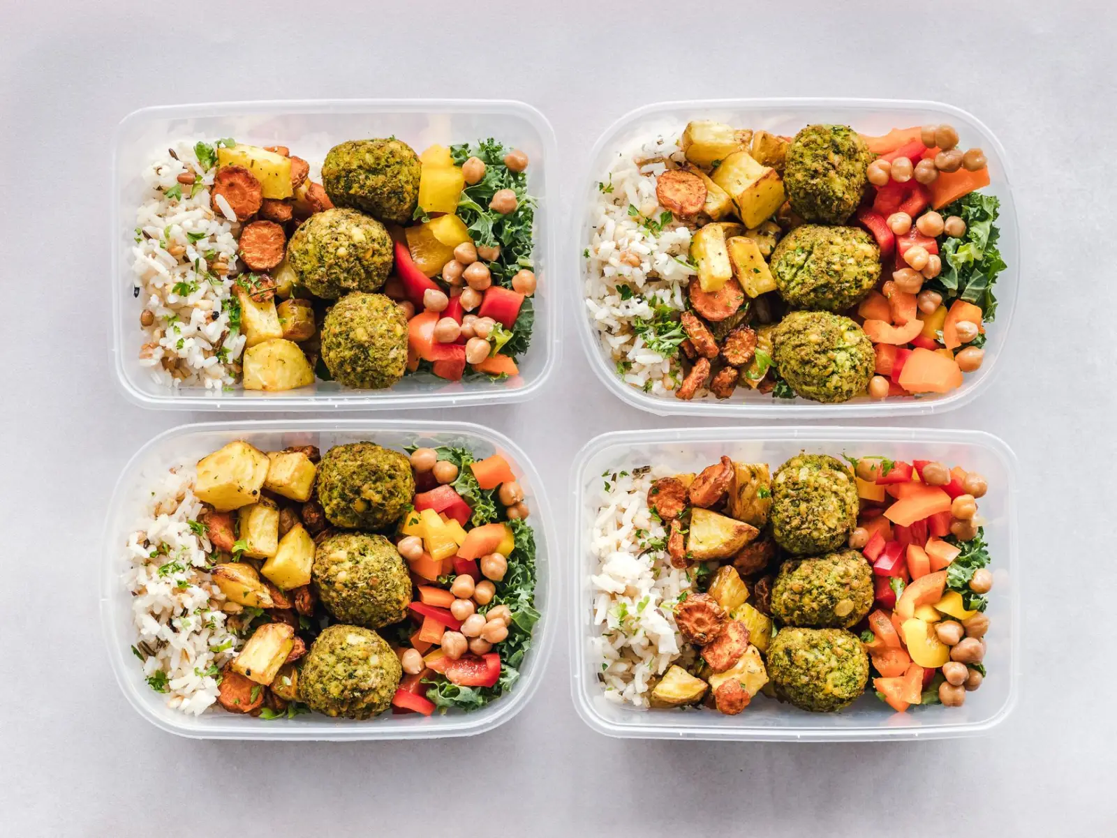 Colorful protein-forward meal-prep containers with grains and vegetables on a white surface.