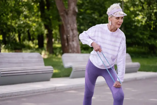 Senior woman performing outdoor exercise with a resistance band in a park.