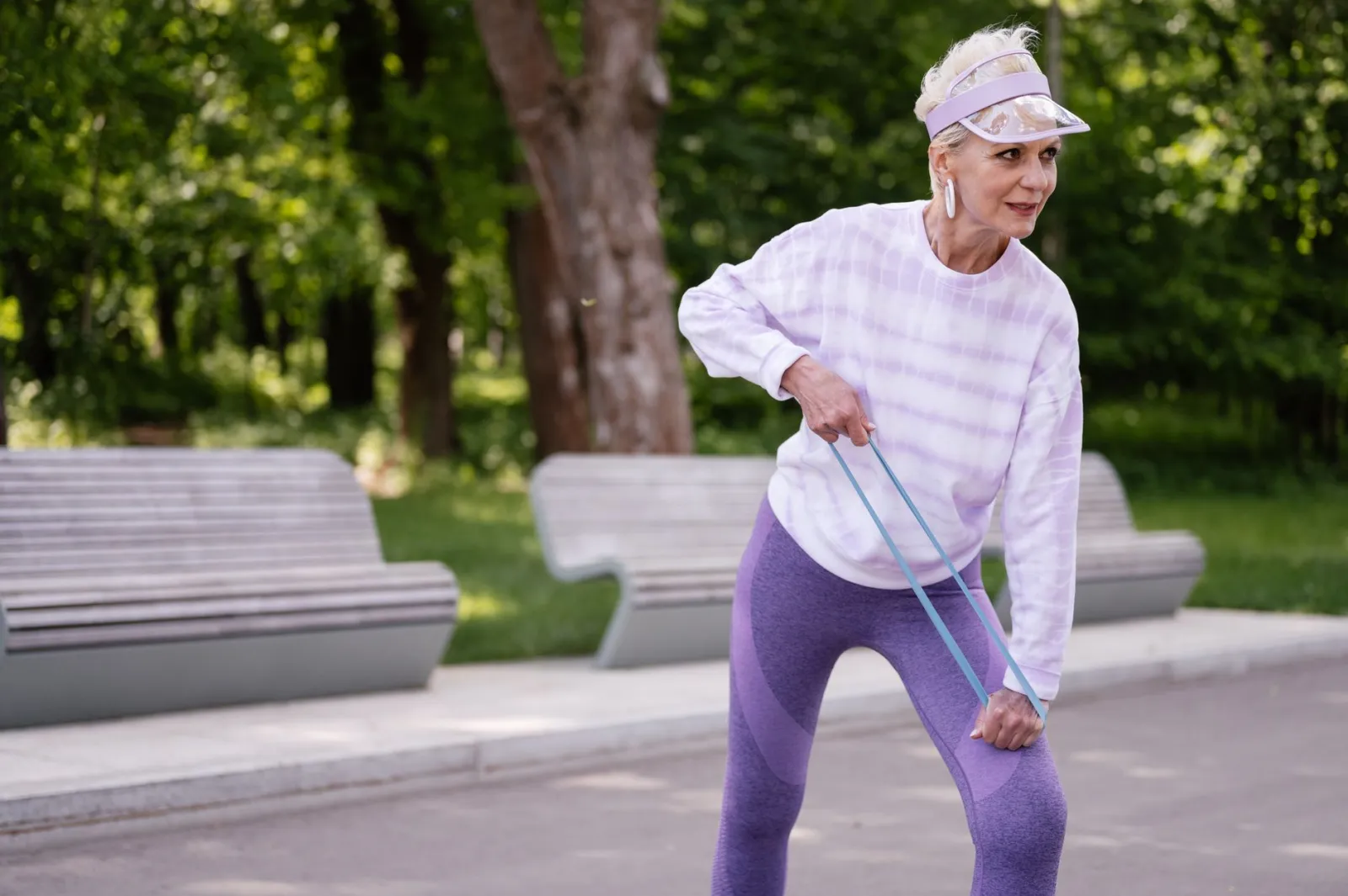 Senior woman performing outdoor exercise with a resistance band in a park setting.