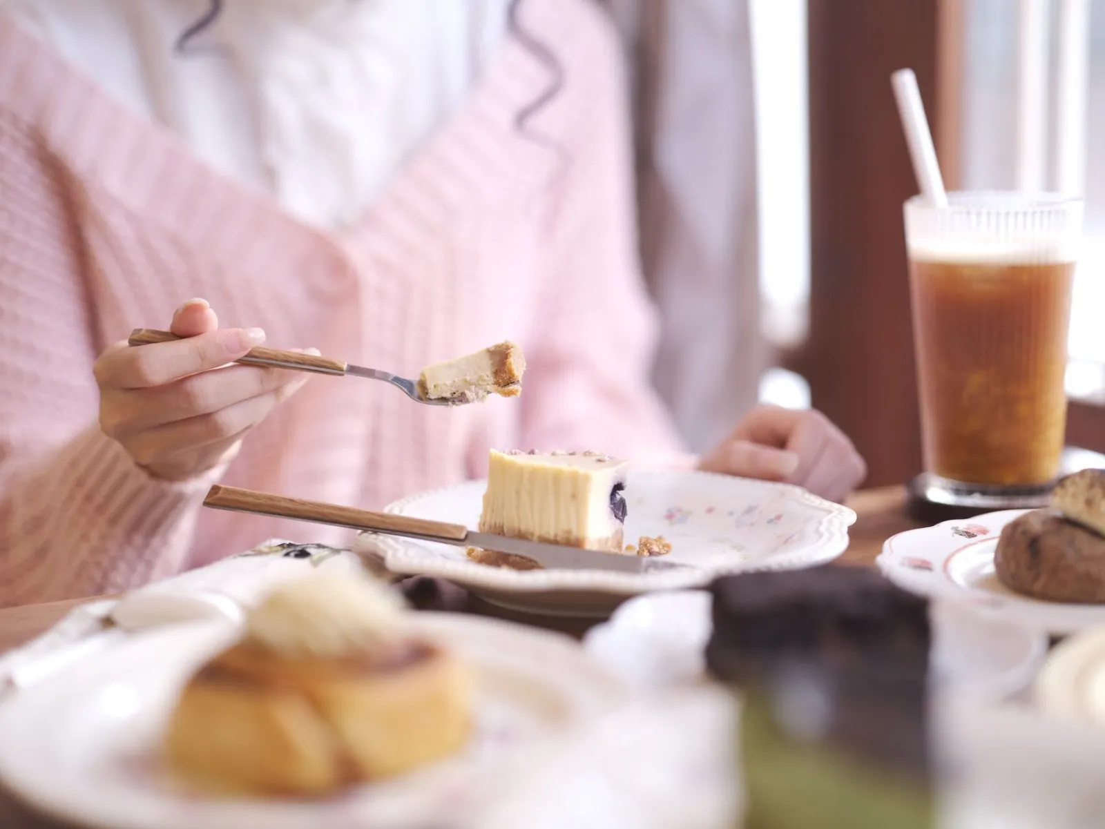 A woman calmly eating a slice of cheesecake with an iced coffee beside her.