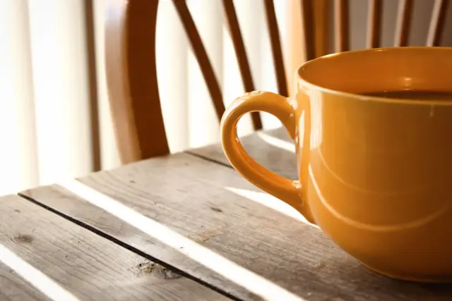 A woman holding coffee in a warm kitchen.