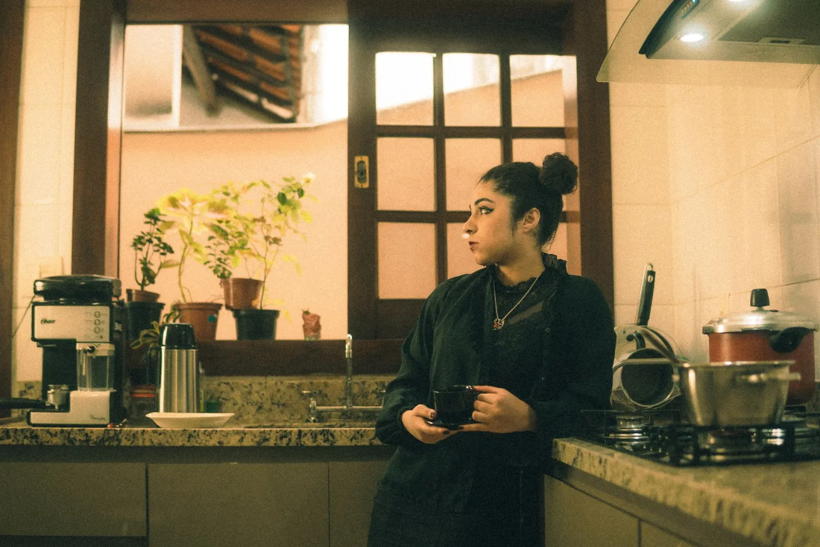 A woman holding coffee in a warm kitchen.