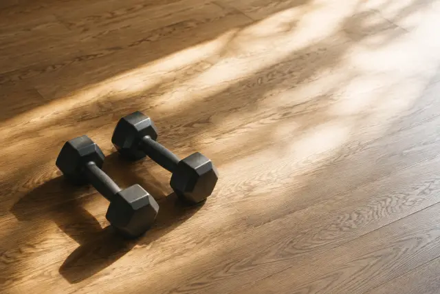 A pair of hex dumbbells resting on a plain floor in natural sunlight.