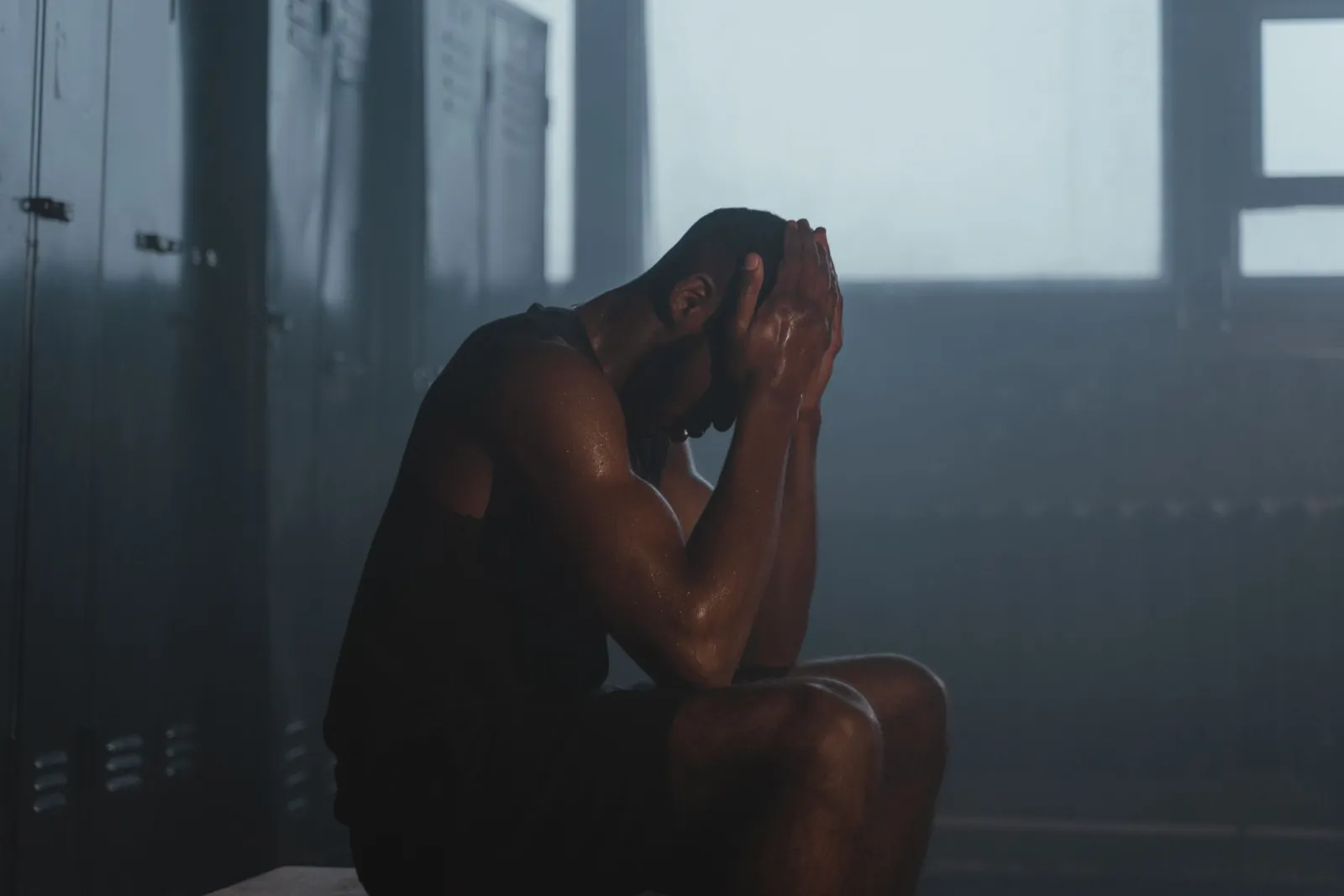 A person sitting on a bench in a dimly lit home gym, resting with a towel over one shoulder.