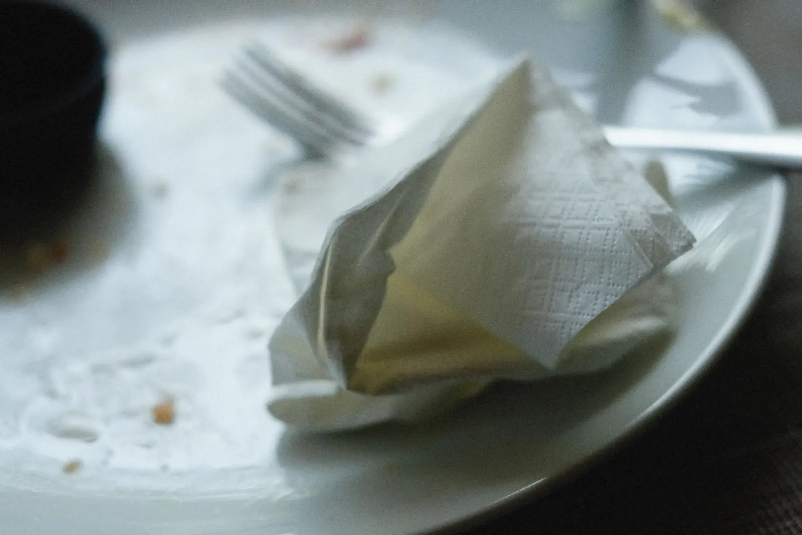An empty plate with a fork and a crumpled napkin on a plain dining table.