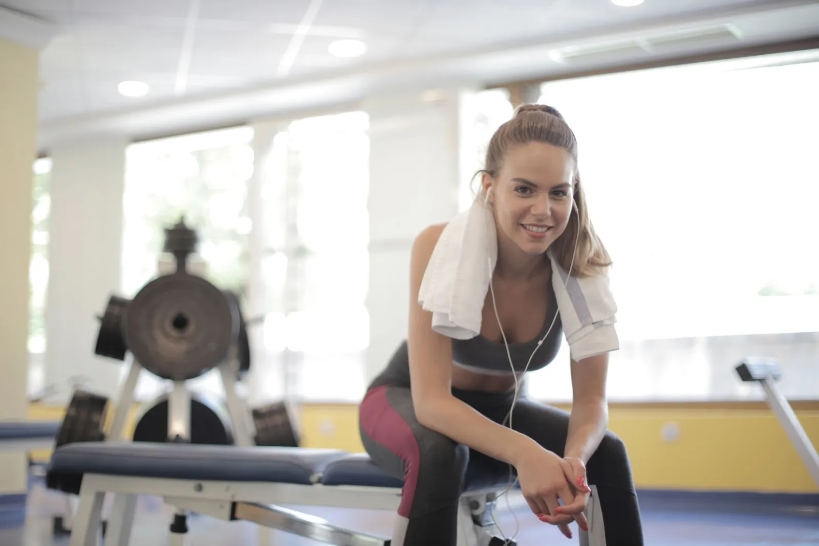 A woman taking a break on a gym bench with a towel and headphones.