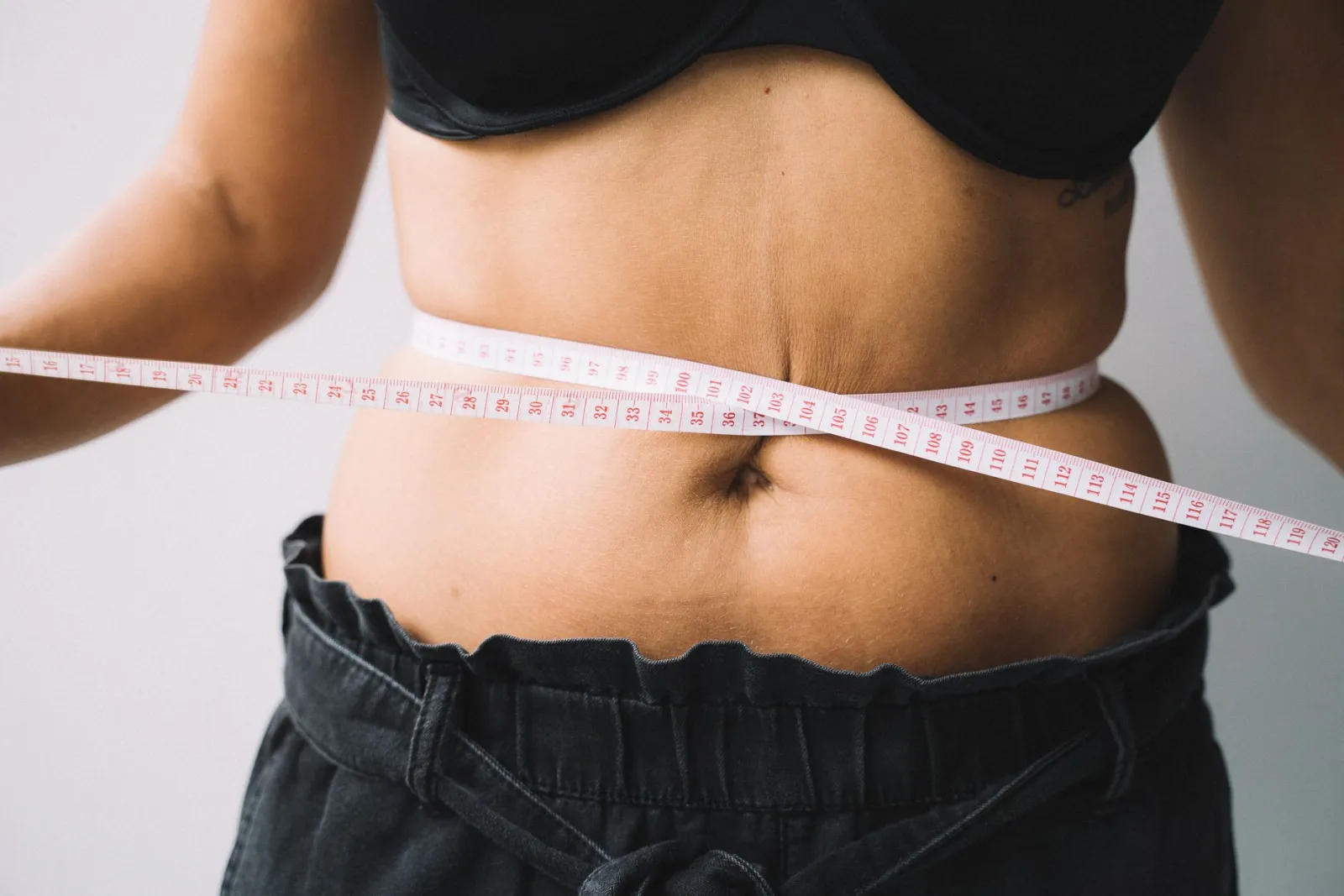 A person measuring their waist with a tape measure.