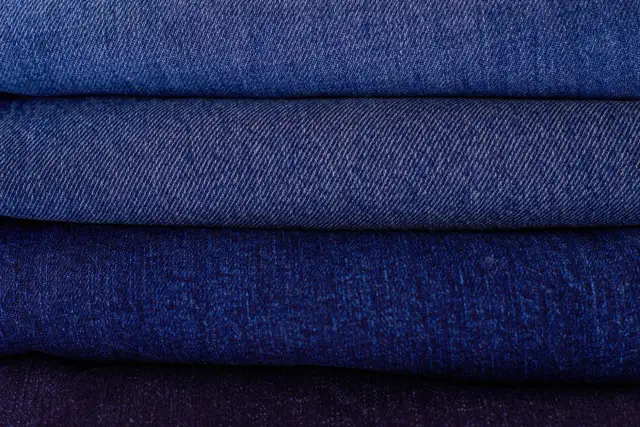 A stack of neatly folded denim jeans in several shades of blue.