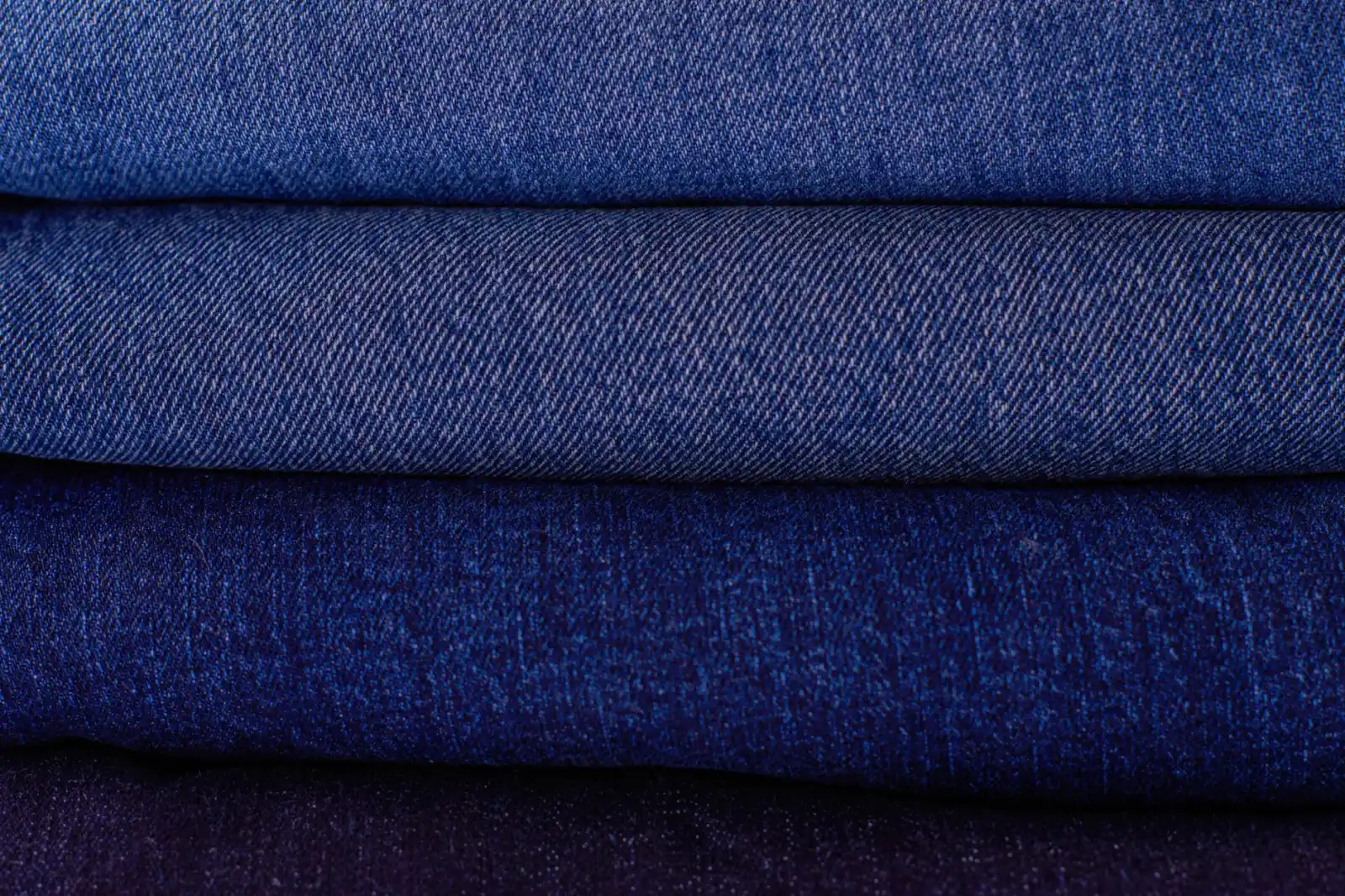 A stack of neatly folded denim jeans in several shades of blue.