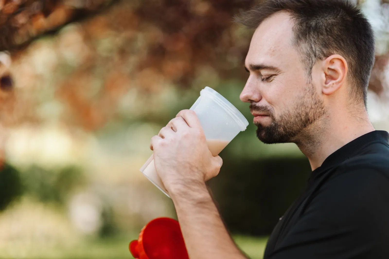 Adult man savoring a protein shake in a peaceful outdoor setting during the day.