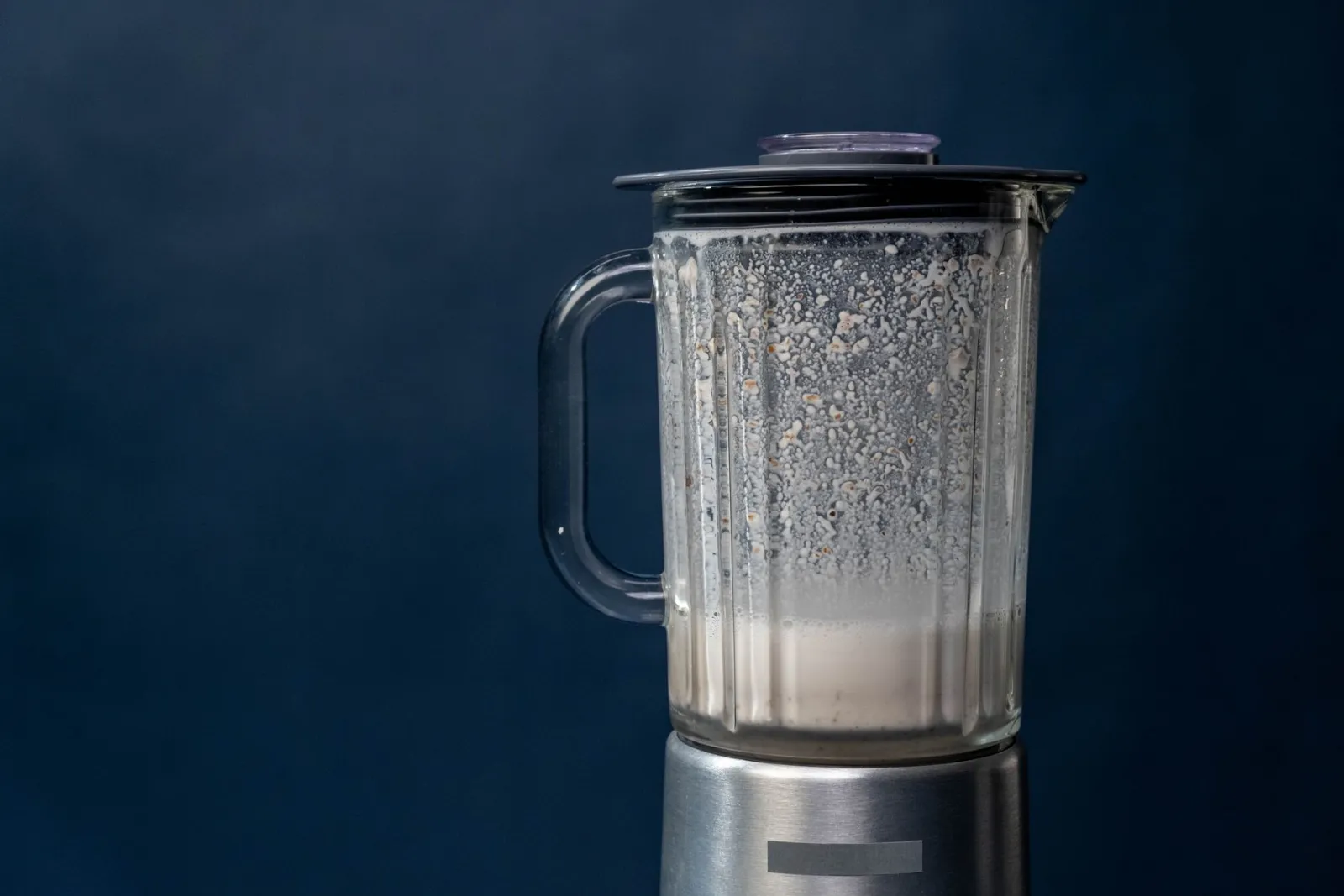 A steel blender jug mixing a milkshake against a plain blue background.