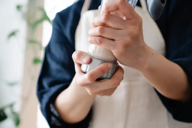 A person shaking a protein shake in a kitchen.